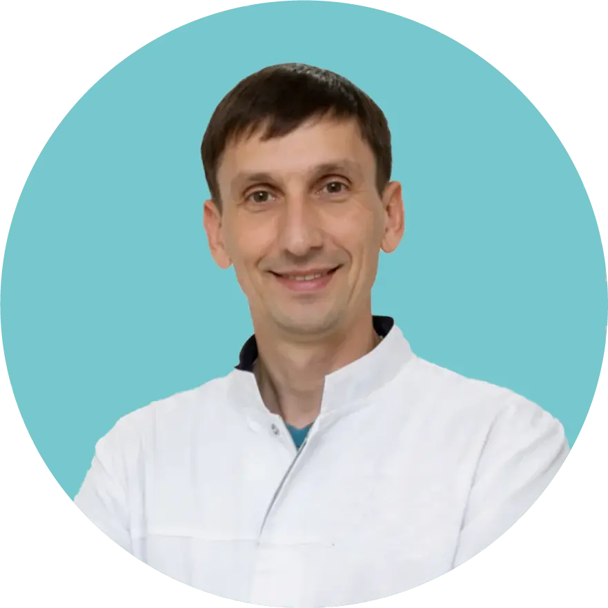 Portrait of a smiling man in a white medical coat against a blue background.